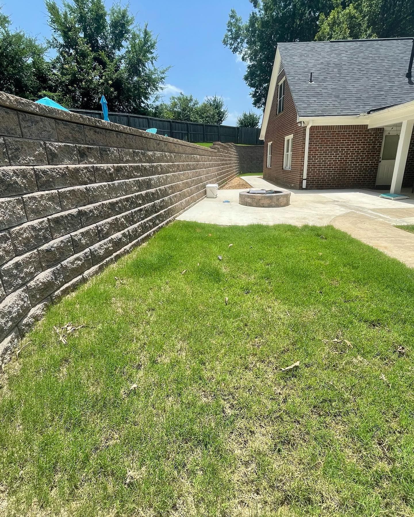 Retaining wall next to a lawn with a house in the background. Fire pit on a concrete patio.