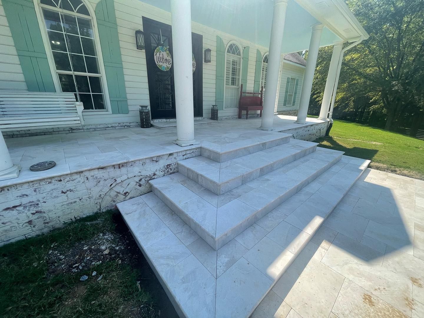 Exterior of a house with light blue porch ceiling, white pillars, and gray stone steps.