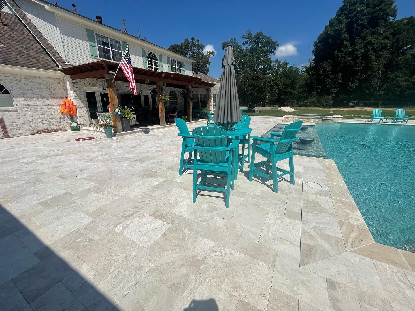Poolside patio with turquoise furniture and a house with shutters under a blue sky.