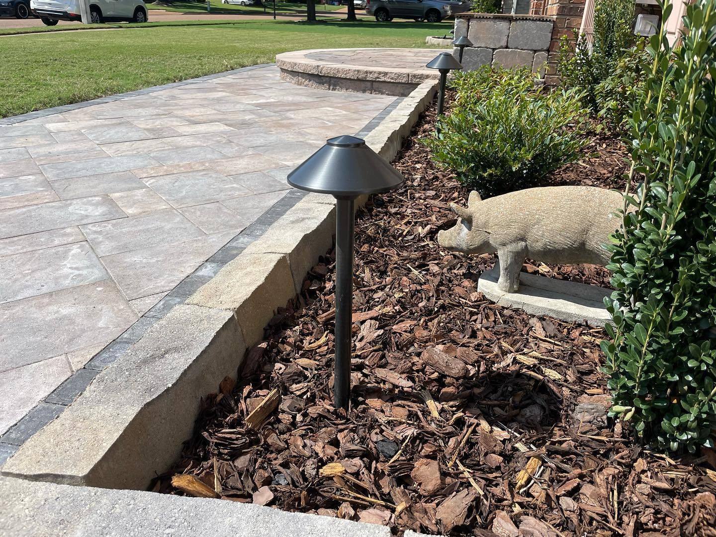 Dark landscape light on black pole in mulch next to stone path and shrubs.