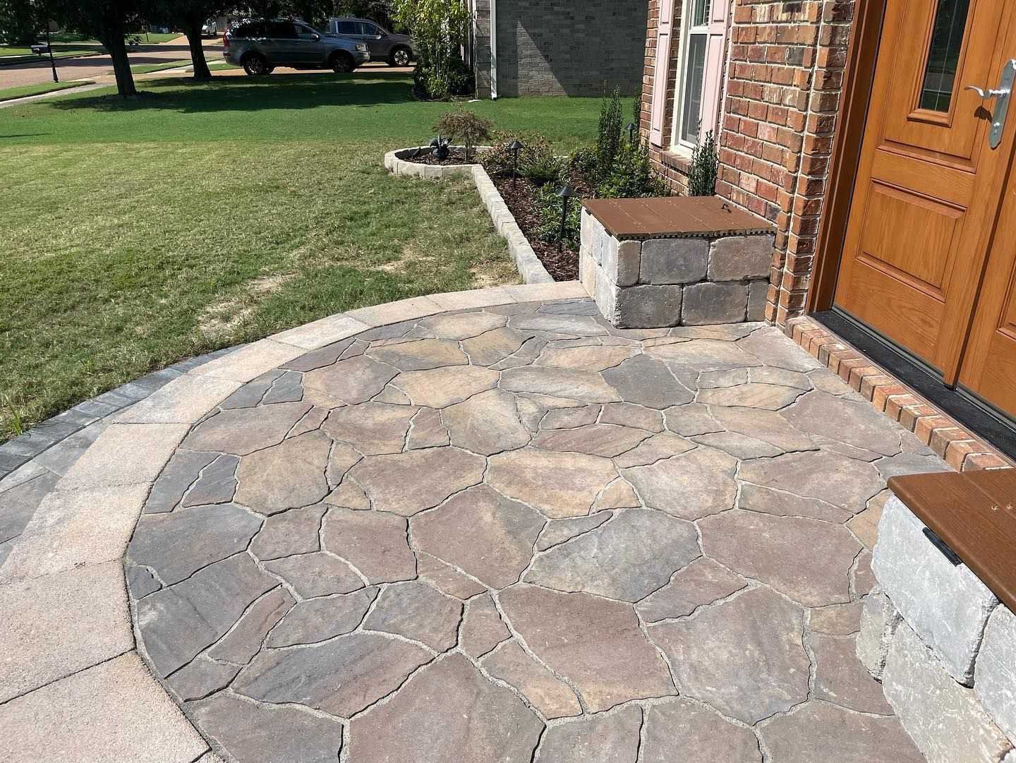 Brick porch and walkway with irregular pavers, leading to a wooden door and adjacent brick building.