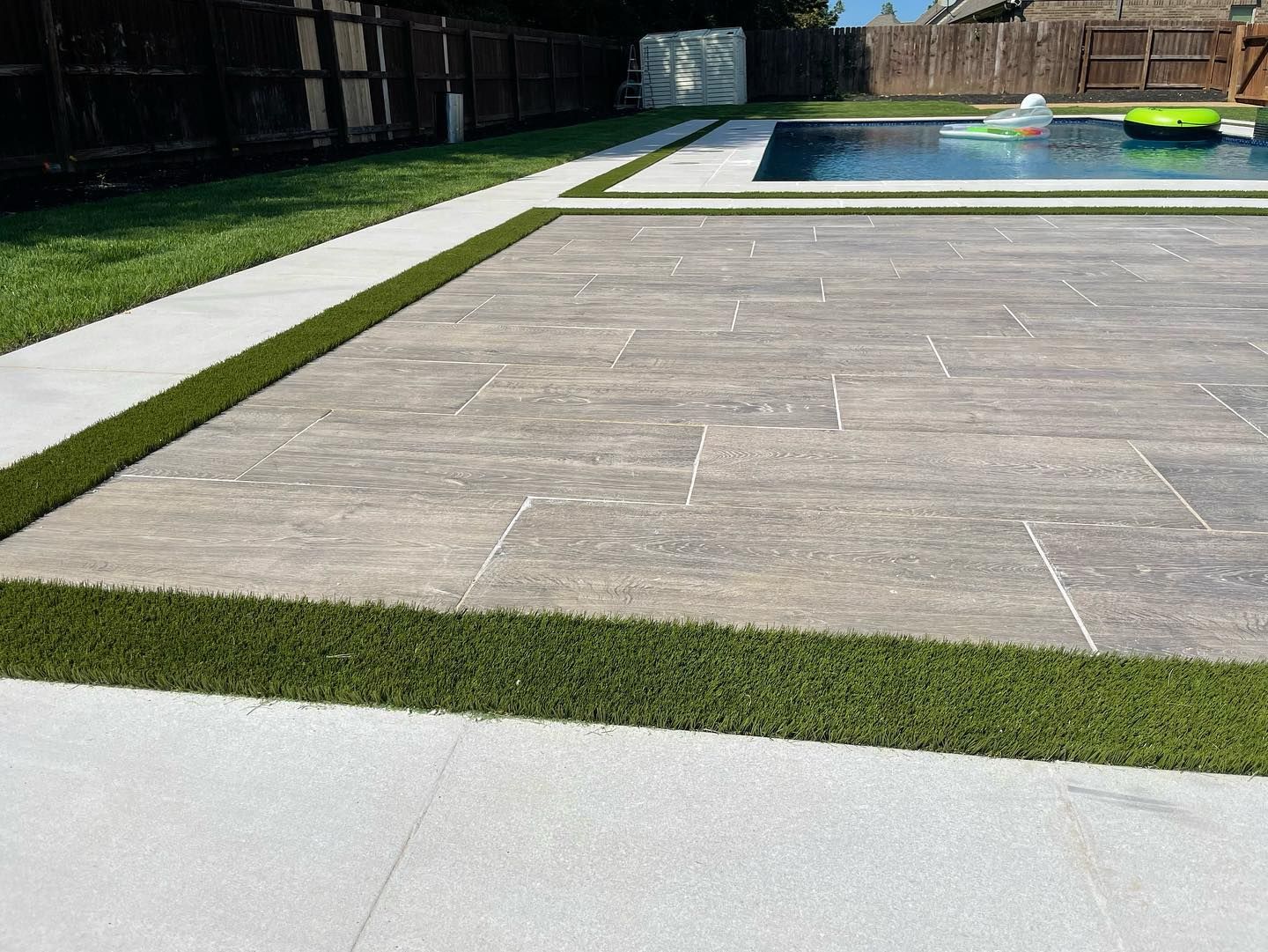 Patio with stone pavers, bordered by artificial turf, leading to a pool.