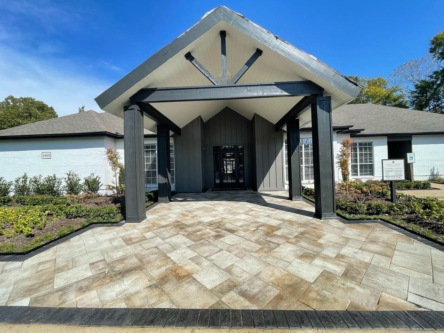 Exterior of a modern building with a covered entranceway; gray and white color scheme; blue sky.