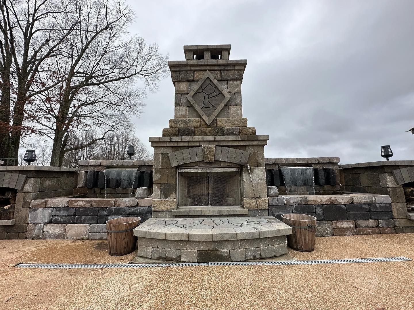 Stone outdoor fireplace with water features and cloudy sky backdrop.