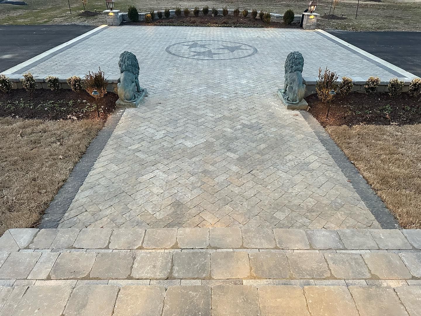 Brick pathway leading to a large stone patio with decorative lion statues.