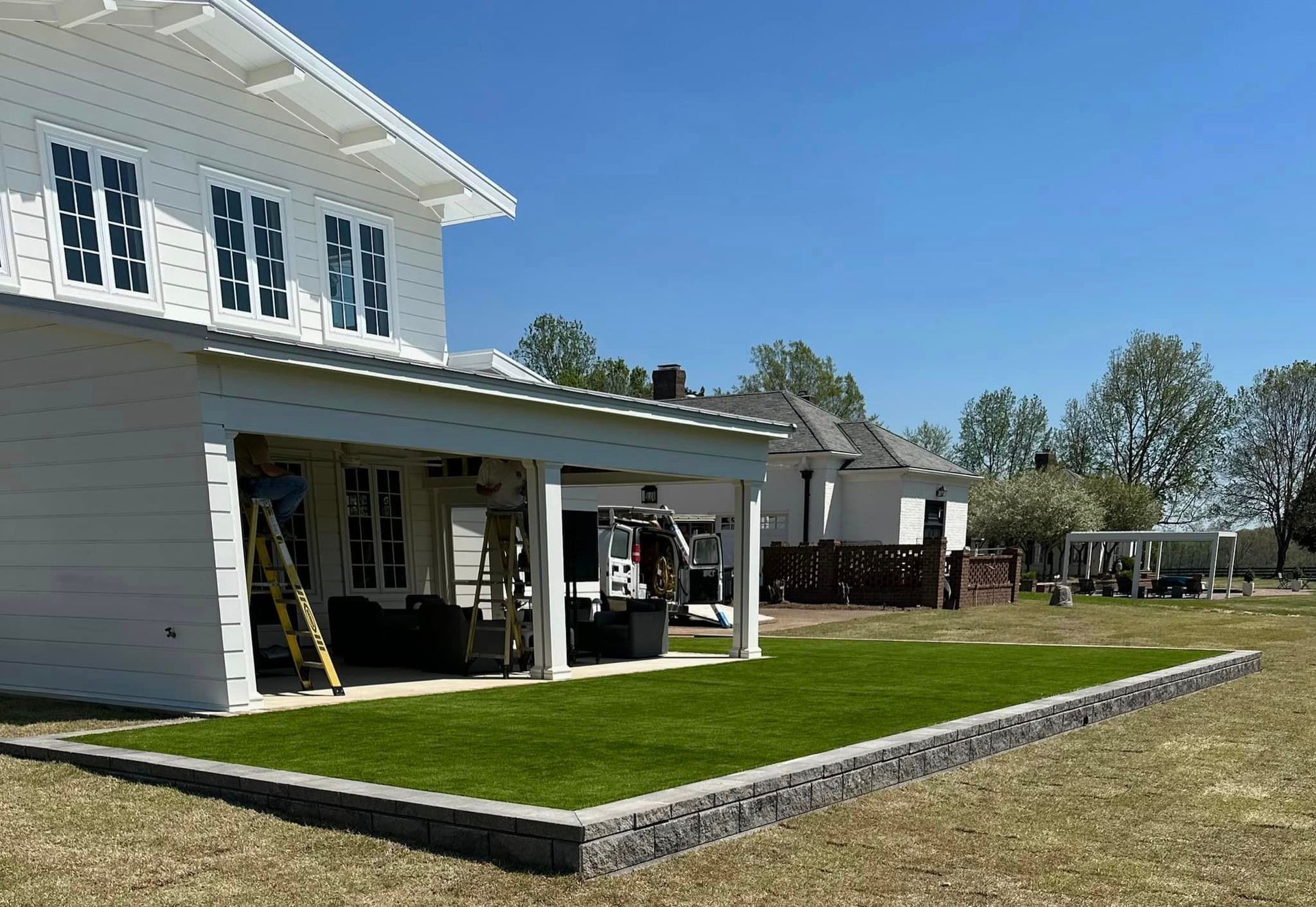 White house with covered porch, retaining wall, and green lawn on a sunny day.