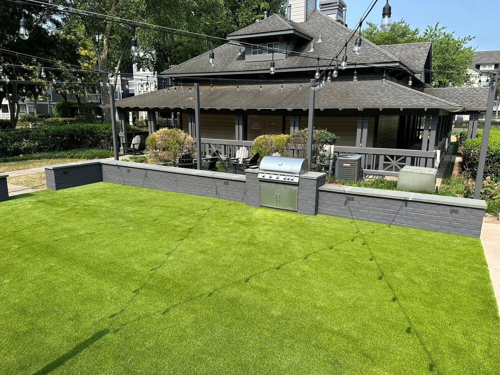 Backyard with a green lawn, grill, and a dark-roofed building in the background.