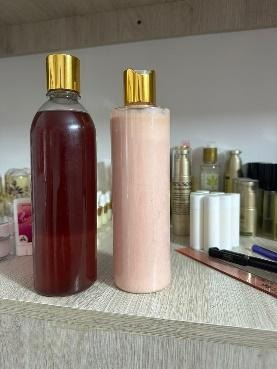 Dos frascos, uno lleno de líquido rojo y el otro de loción rosa, ambos con tapones dorados, sobre un estante.