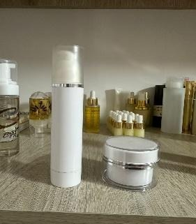 Productos blancos para el cuidado de la piel: frasco con dosificador y tarro con detalles plateados en un estante.