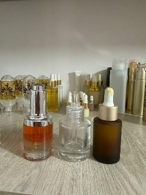 Tres frascos de sérum cosmético en un estante: uno transparente, uno ámbar y uno vacío, con goteros.