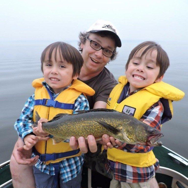 Photo of a man with two boys holding a freshly caught fish