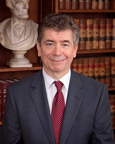 A man in a suit and tie is standing in front of a bookshelf.