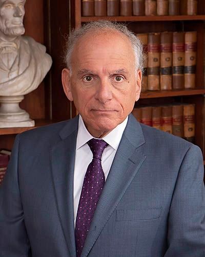 A man in a suit and tie is standing in front of a bookshelf.