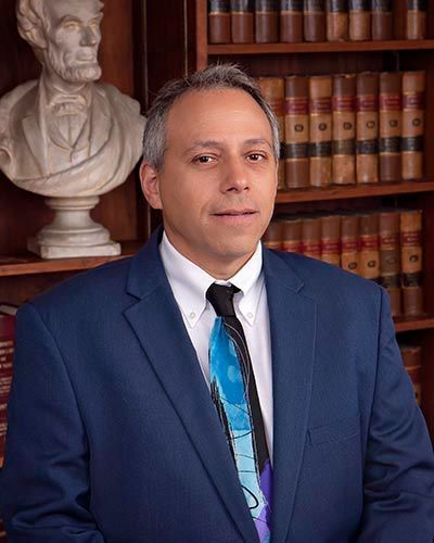 A man in a suit and tie is standing in front of a bookshelf.