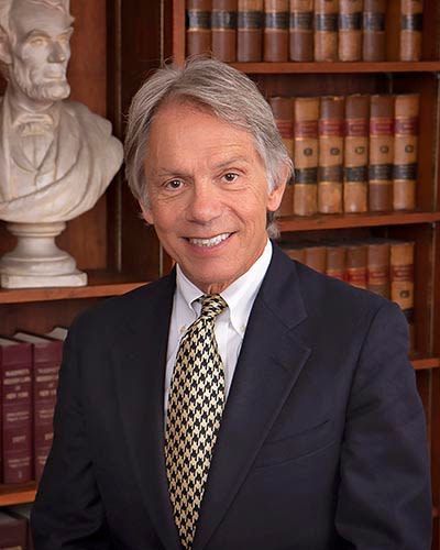 A man in a suit and tie is standing in front of a bookshelf.