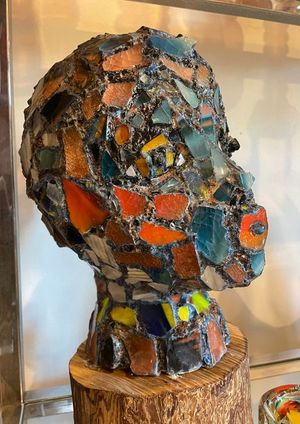 A statue of a mosaic head is sitting on a wooden stump.