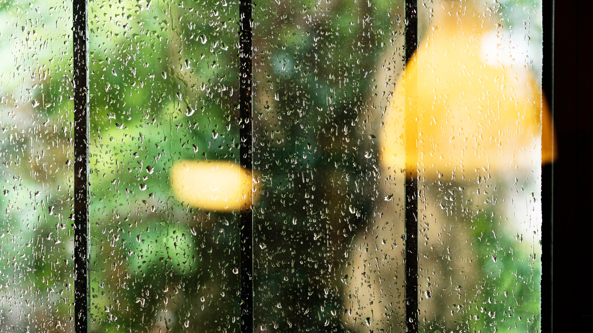 A window with rain drops on it and a lamp in the background.
