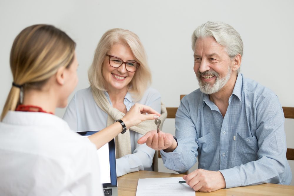 A Woman is Giving a Man and Woman a Set of Keys — All About Conveyancing Taree In Taree, NSW