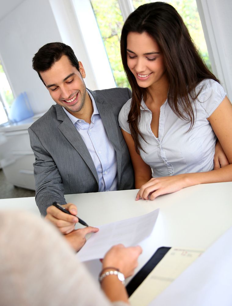 A Man and a Woman Are Sitting at a Table Signing a Document — All About Conveyancing Taree In Harrington, NSW