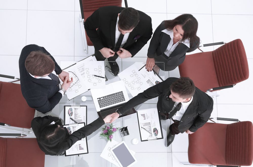 A Group of Business People Are Sitting Around a Table Shaking Hands — All About Conveyancing Taree In Nabiac, NSW