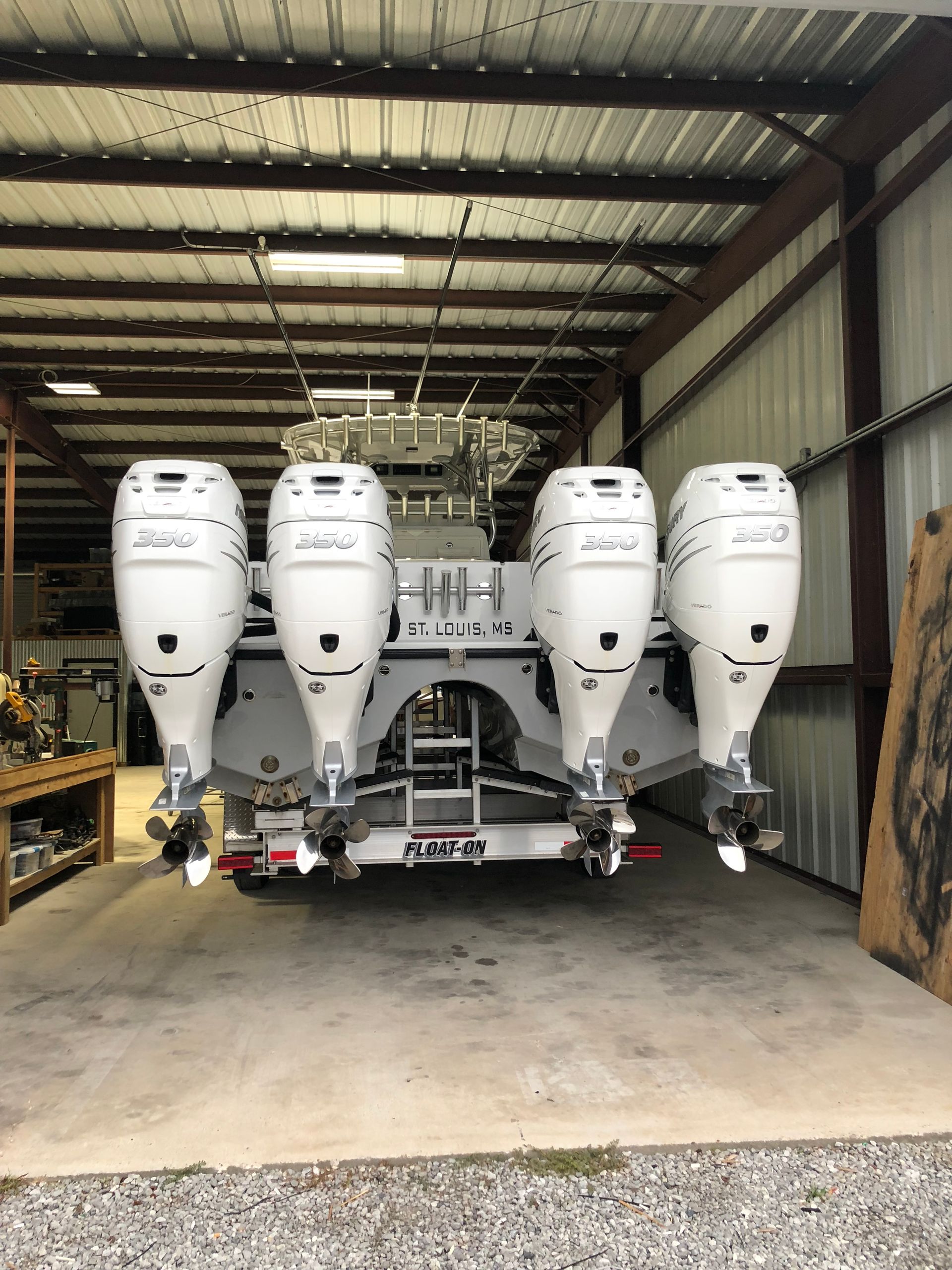 White boat with four large outboard motors inside a garage-like building.