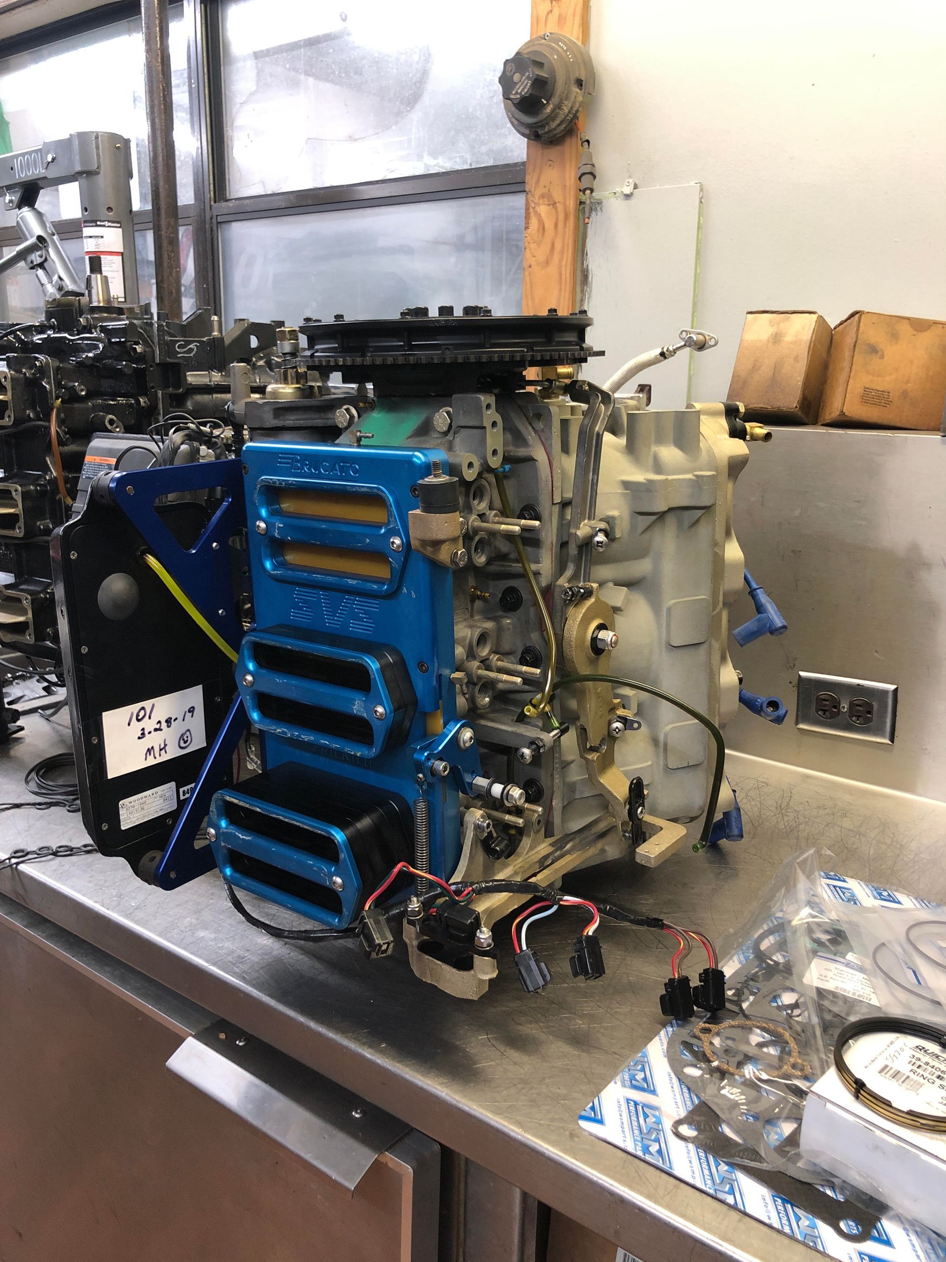 Blue and gray mechanical device on a metal surface, possibly for a vehicle, with wiring and other parts.