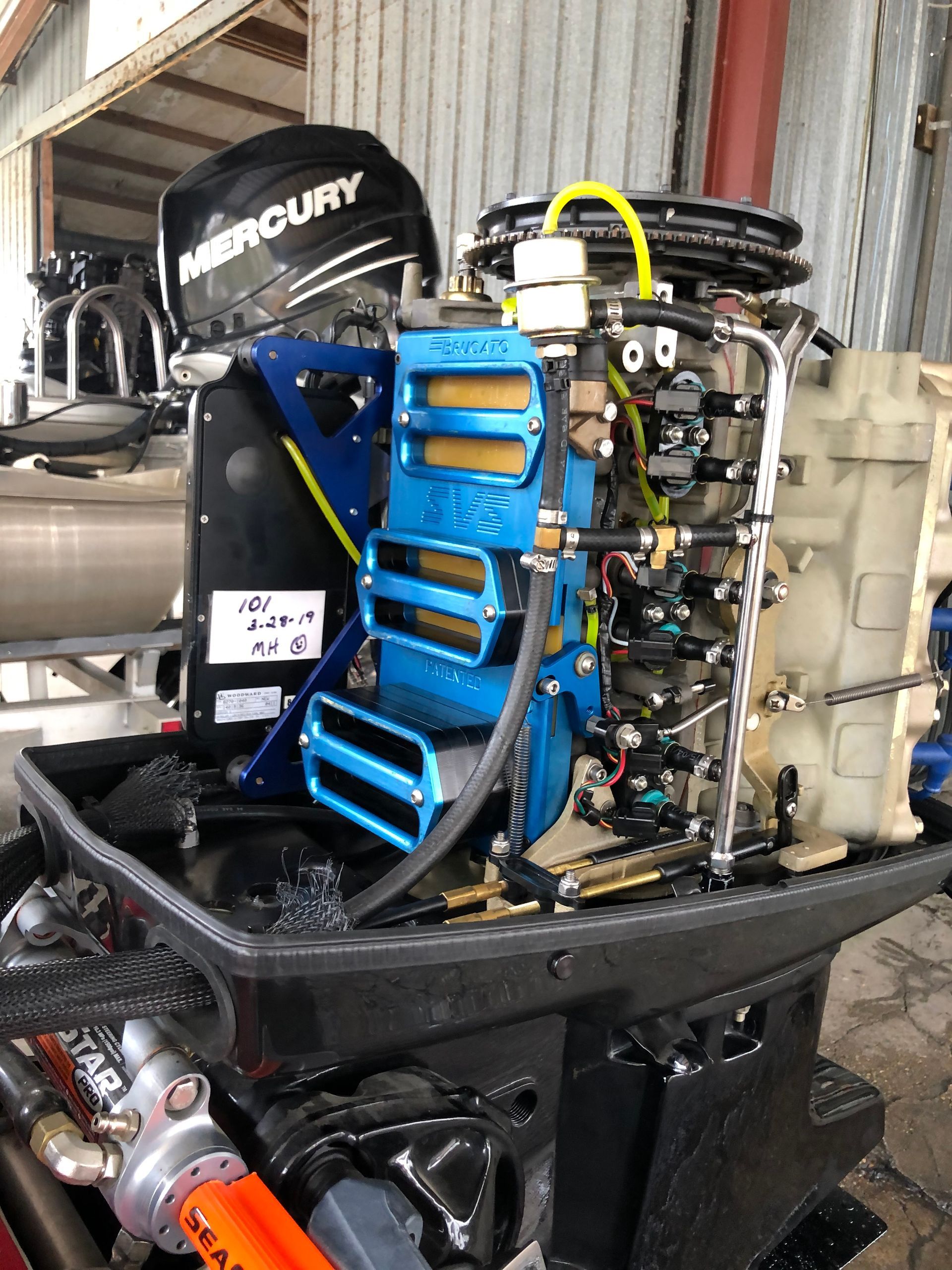 Mercury outboard motor, blue and black, in a shop setting.