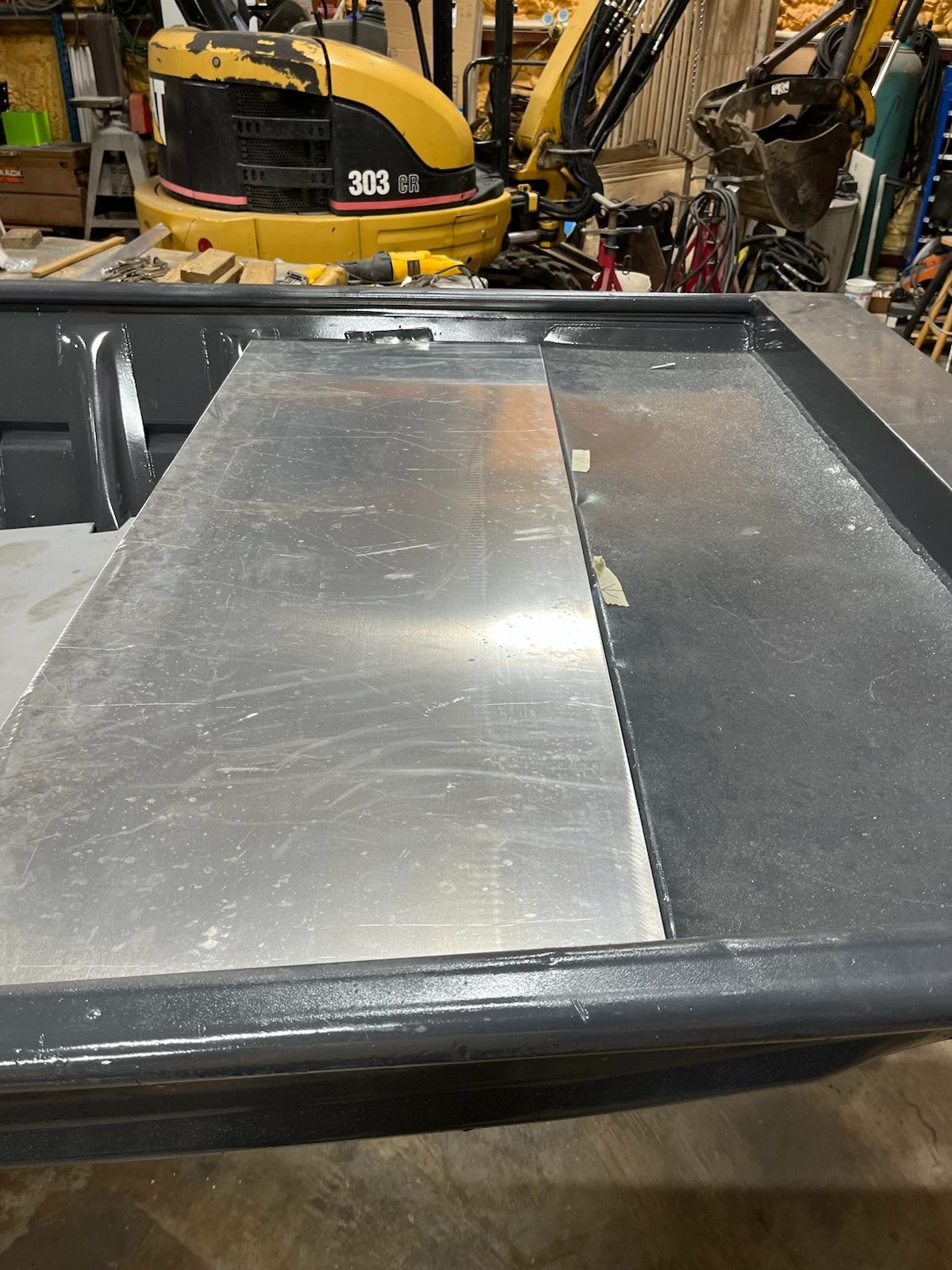Aluminum sheet partially covering a dark gray boat's interior, likely for repair or modification. Workshop setting.