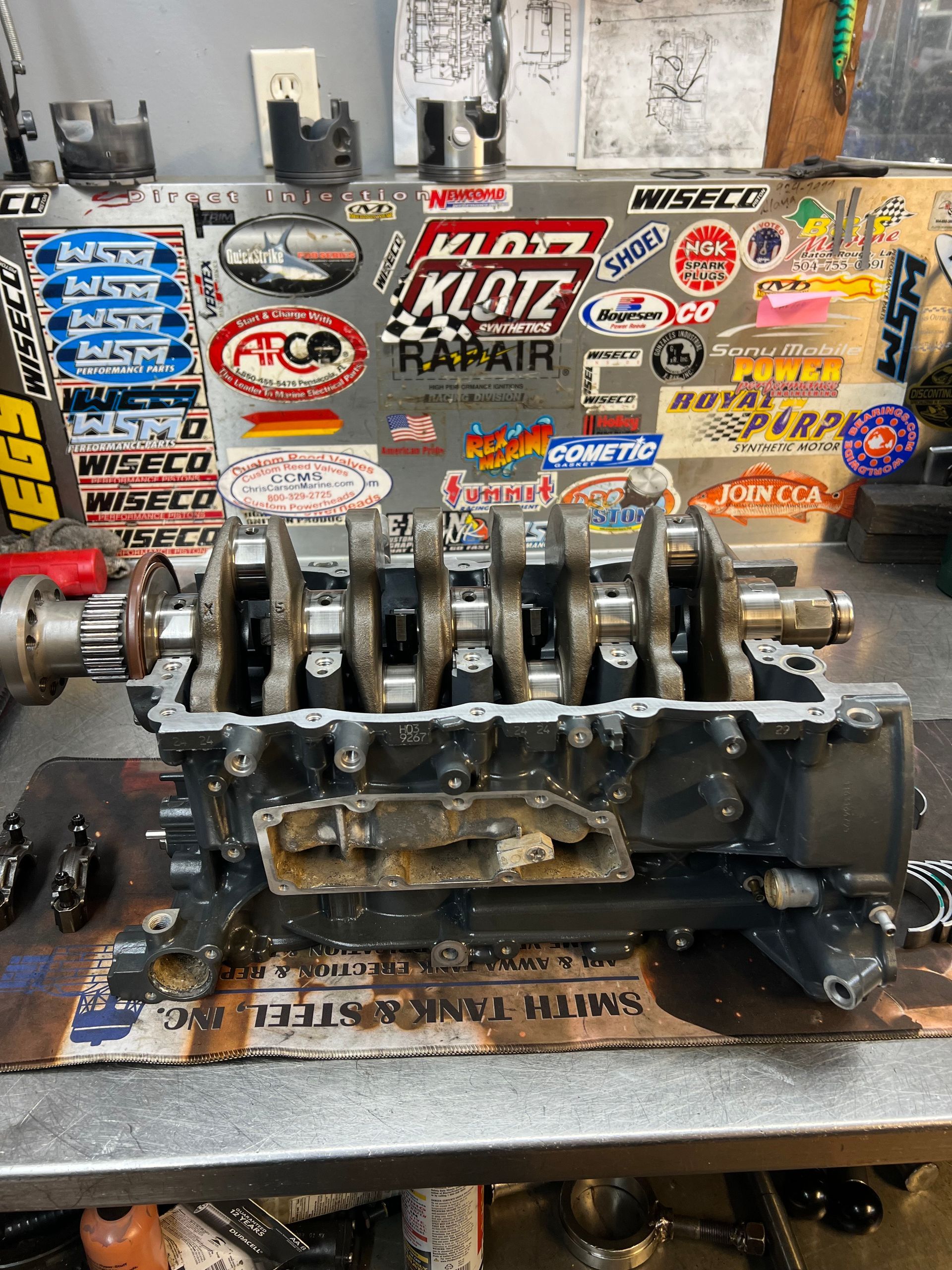 Person painting red underside of a boat on stands, wearing a respirator.