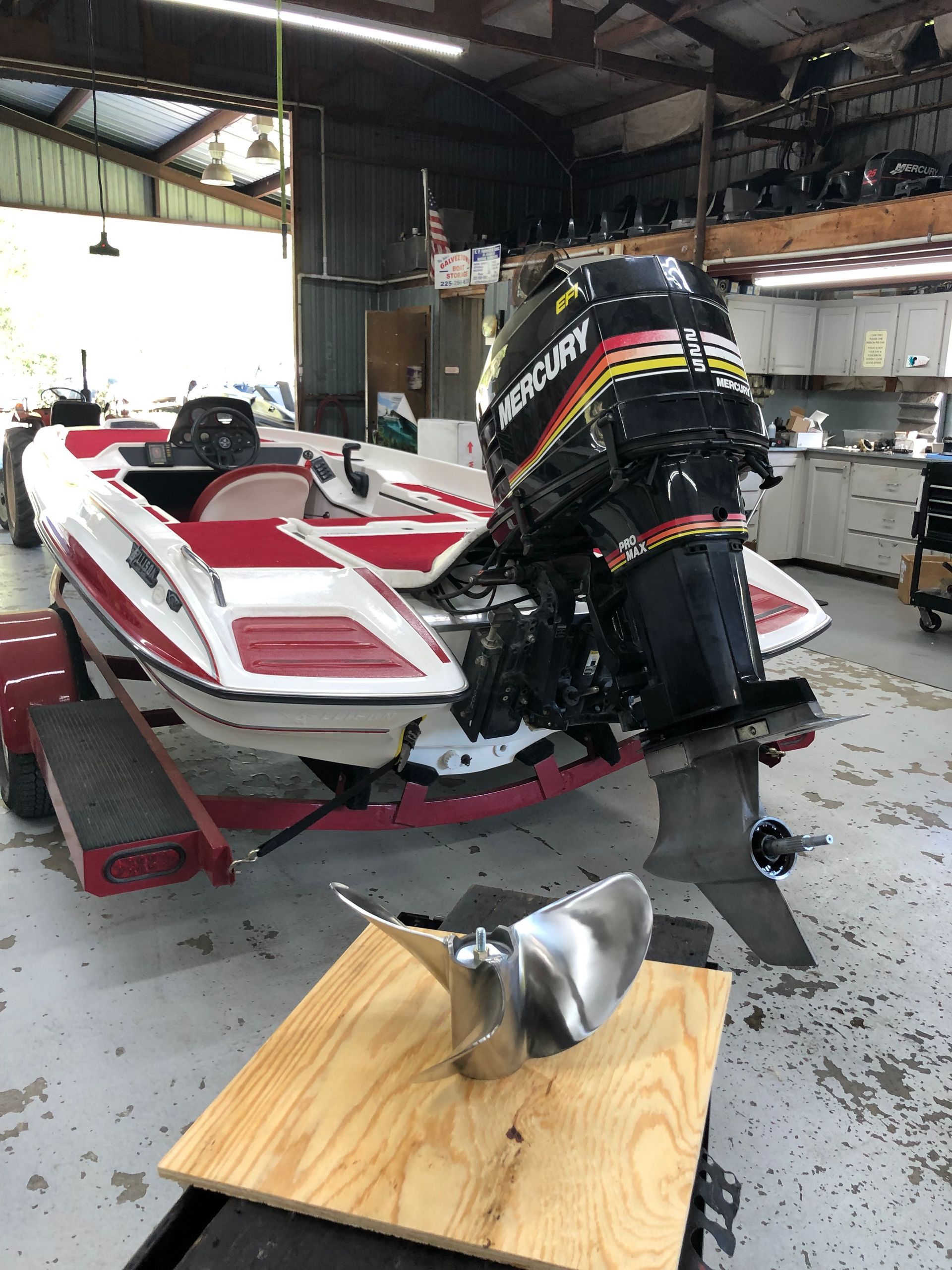 Boat with a Mercury outboard motor in a repair shop, propeller on a wooden board.