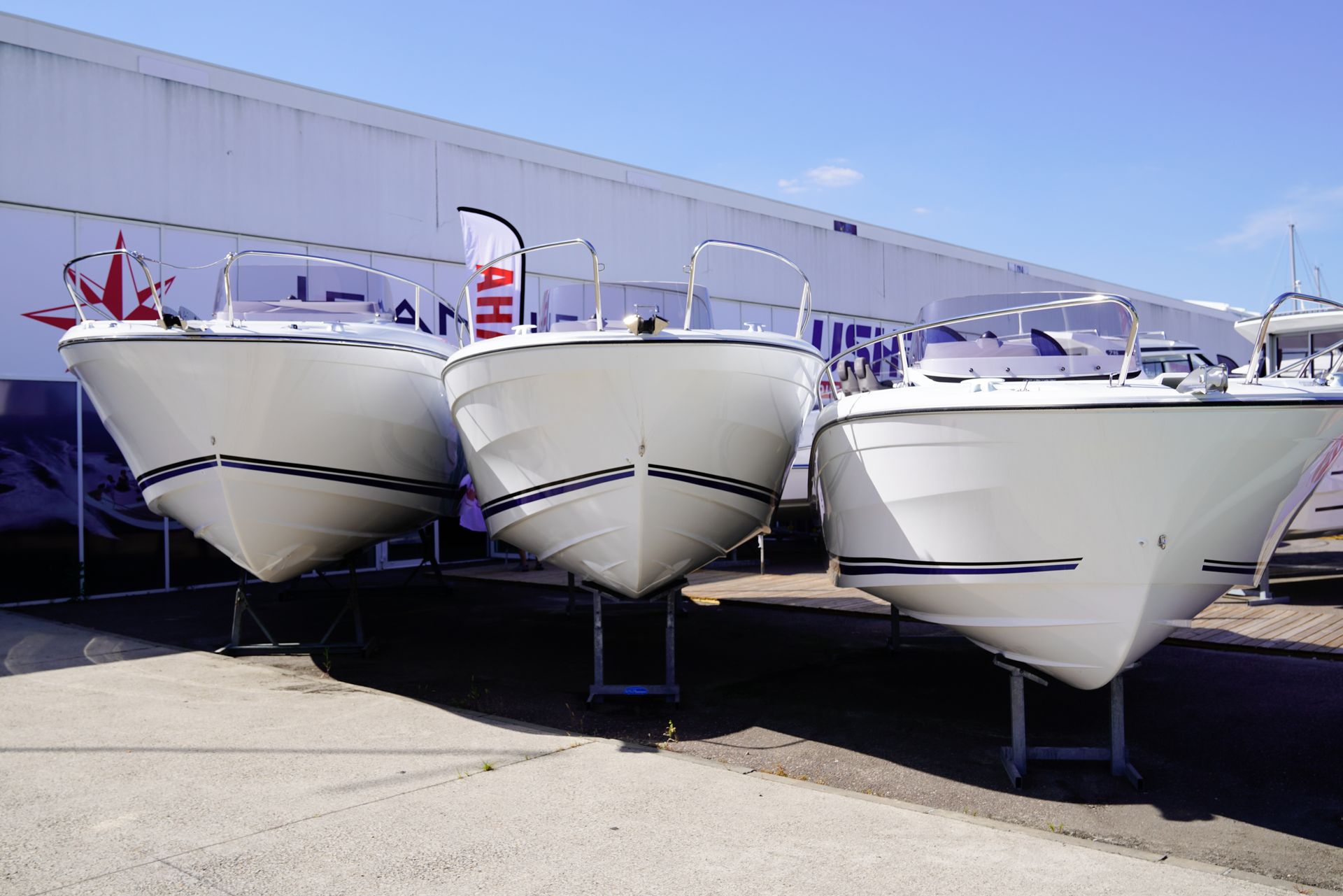 Three white boats on stands in front of a building with blue sky.