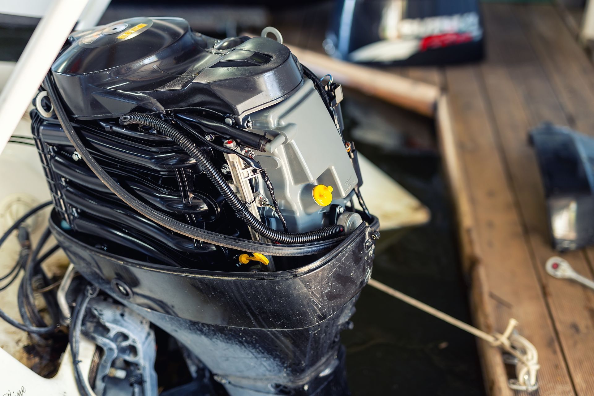 Black boat motor with surrounding wires, on a wooden dock next to water.