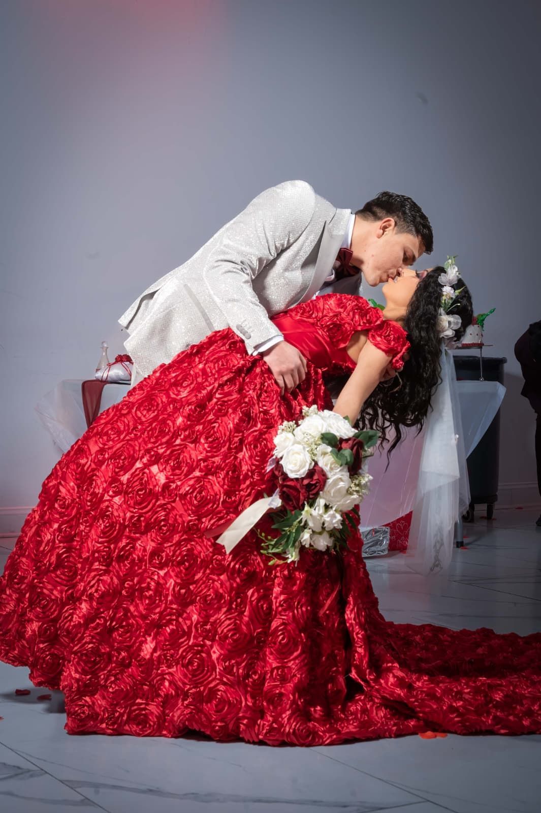 Newlyweds holding marriage license; woman in wedding dress, man in cowboy hat, decorated backdrop.