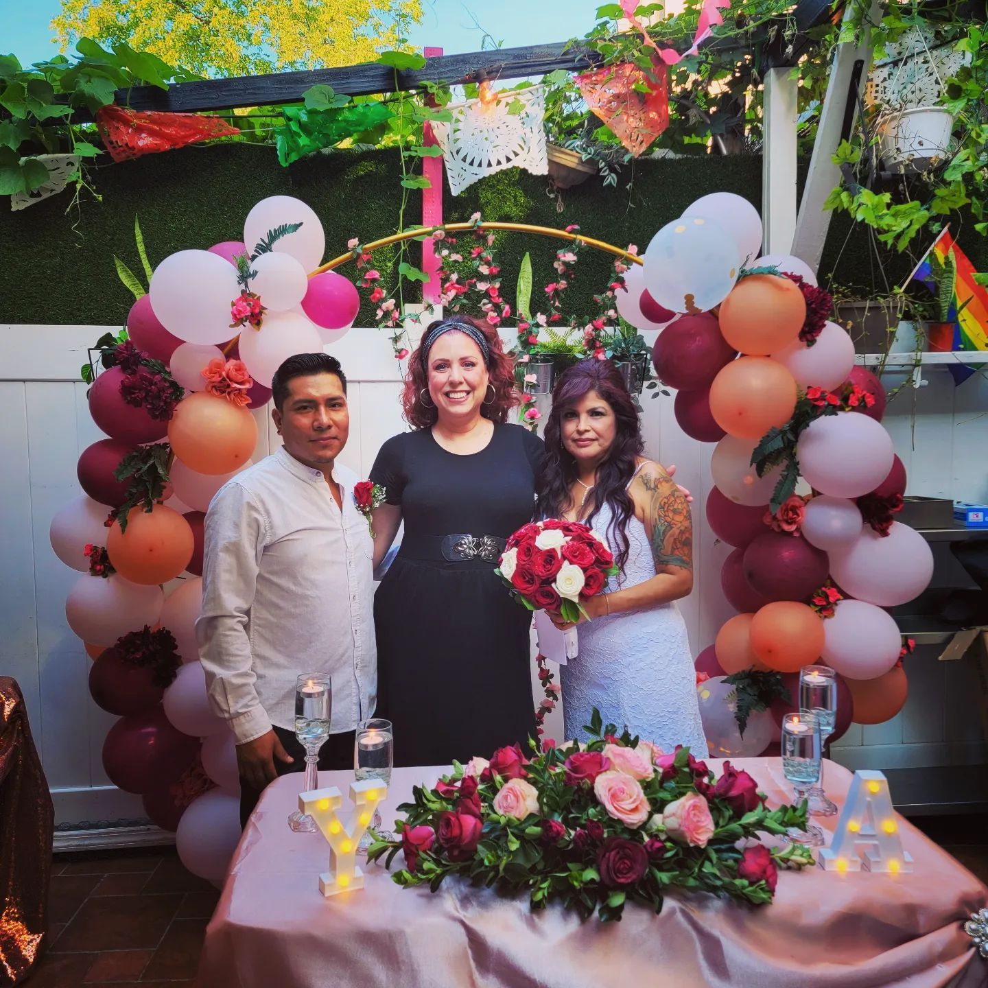 Wedding ceremony: Three people stand behind a table with flowers, decorated with balloons.