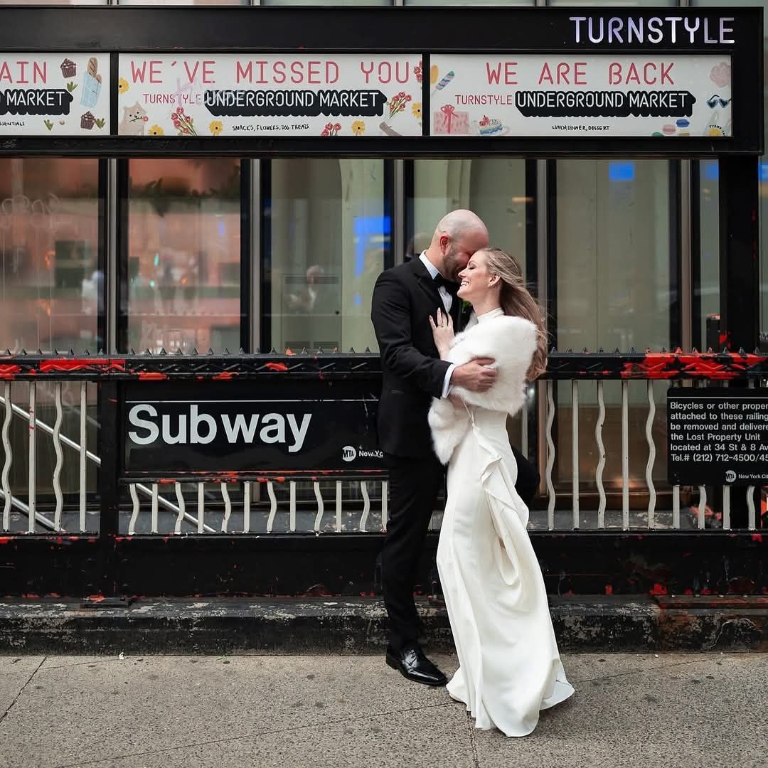 Couple kissing in a dip, bride in red dress holding flowers, groom in silver suit. White floral headpiece and veil.