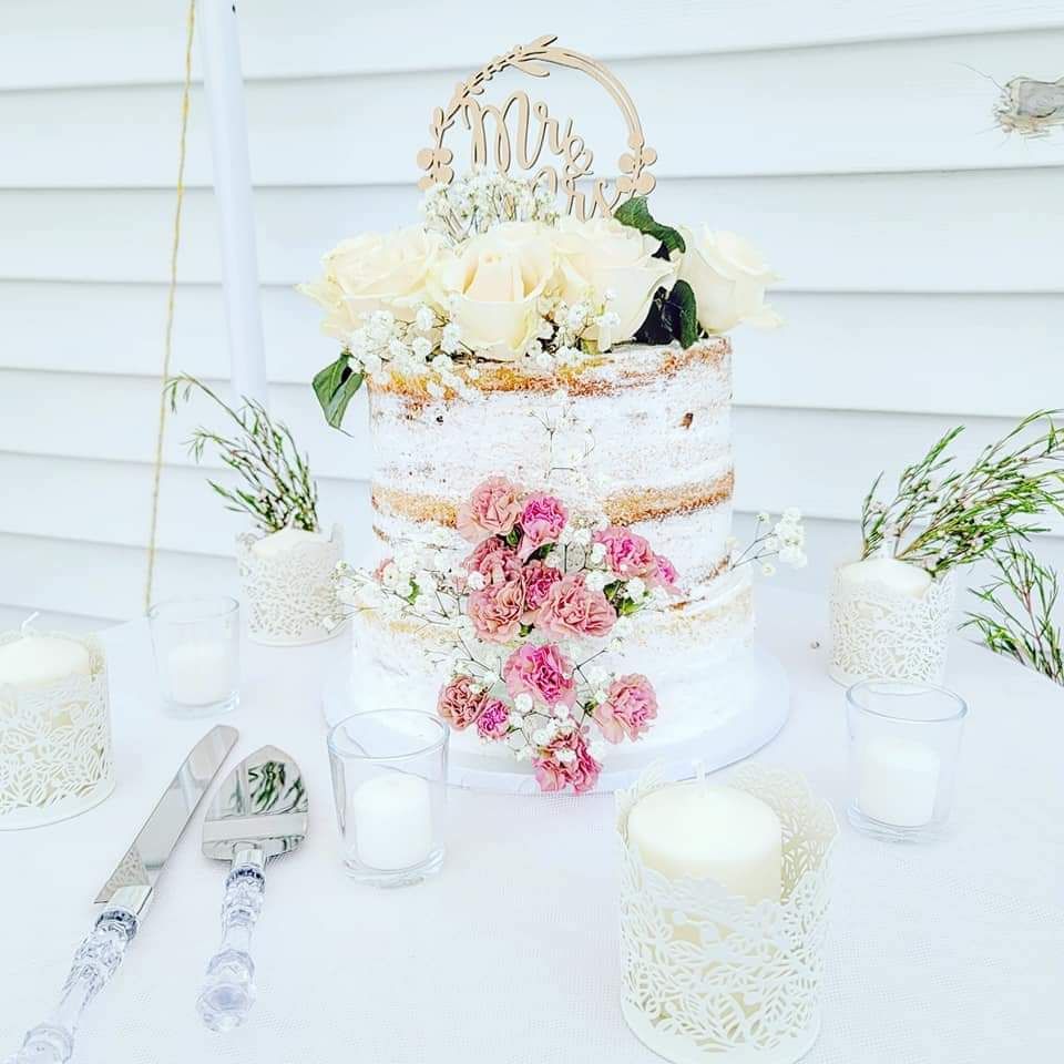 A two-tiered semi-naked wedding cake topped with white roses and a 