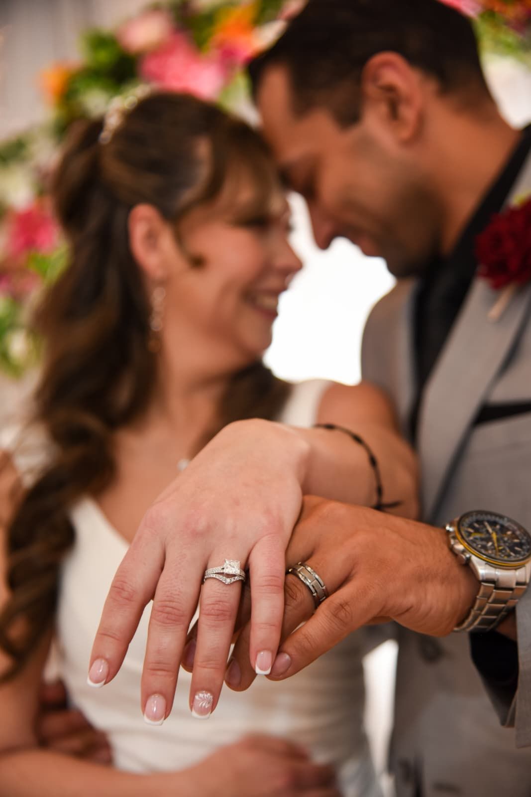 Wedding ceremony. Bride and groom face officiant; bridal party and groomsmen watch. Wooden backdrop.
