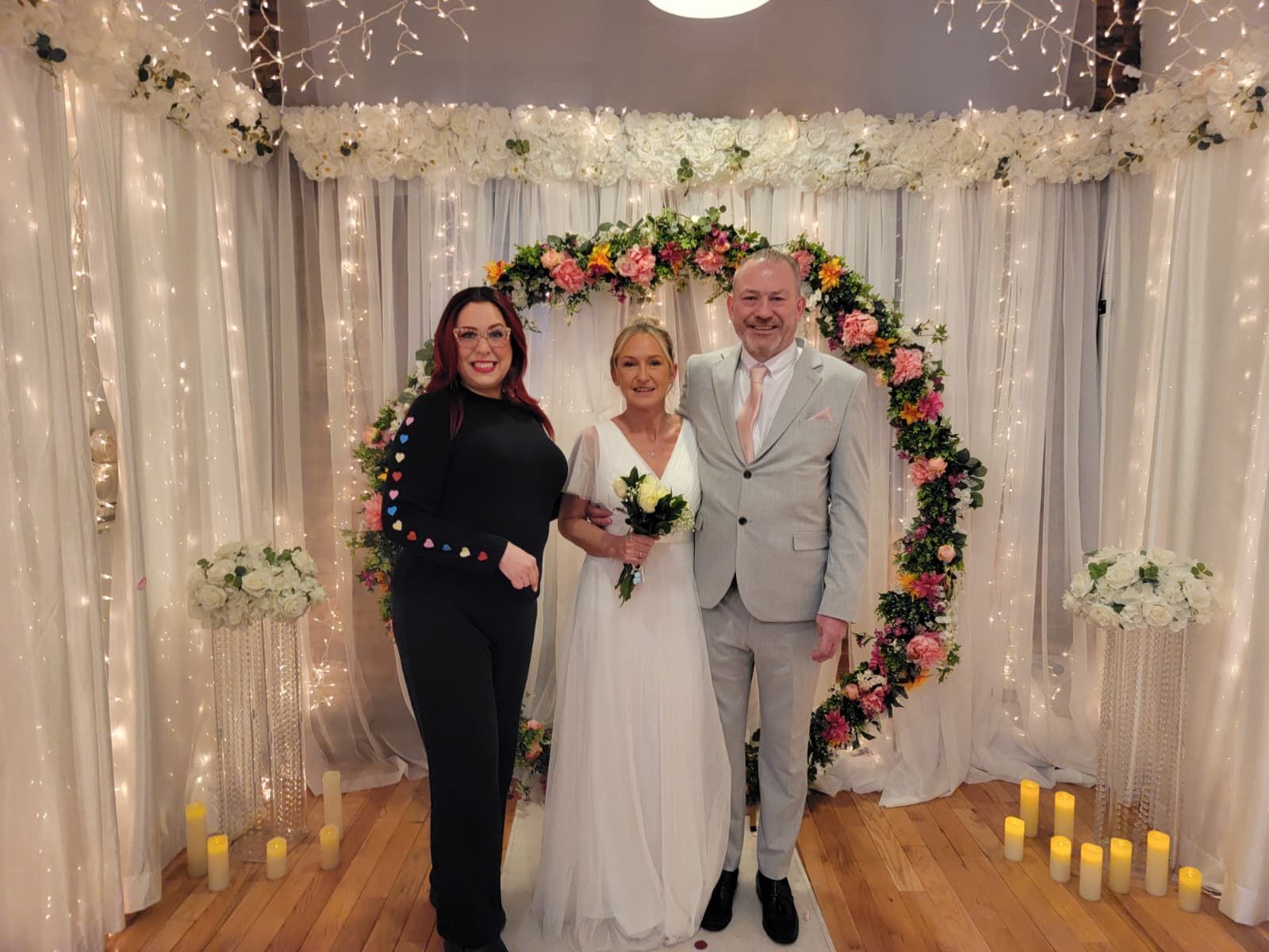 Bride signing wedding documents with groom and witness on a white bench outdoors.