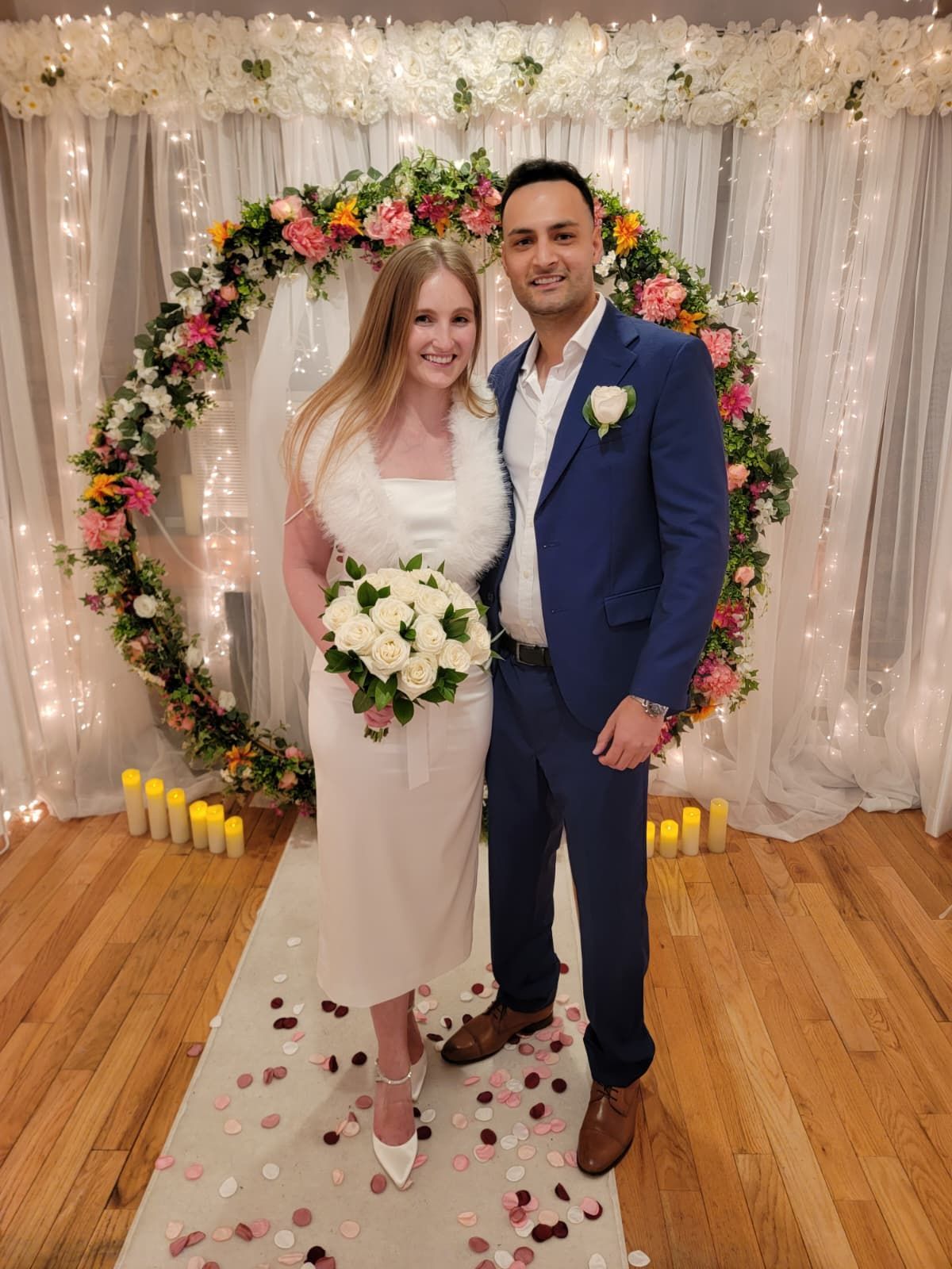 Woman singing at an outdoor wedding. She's wearing a black dress, black tights, and standing under a decorated arch.