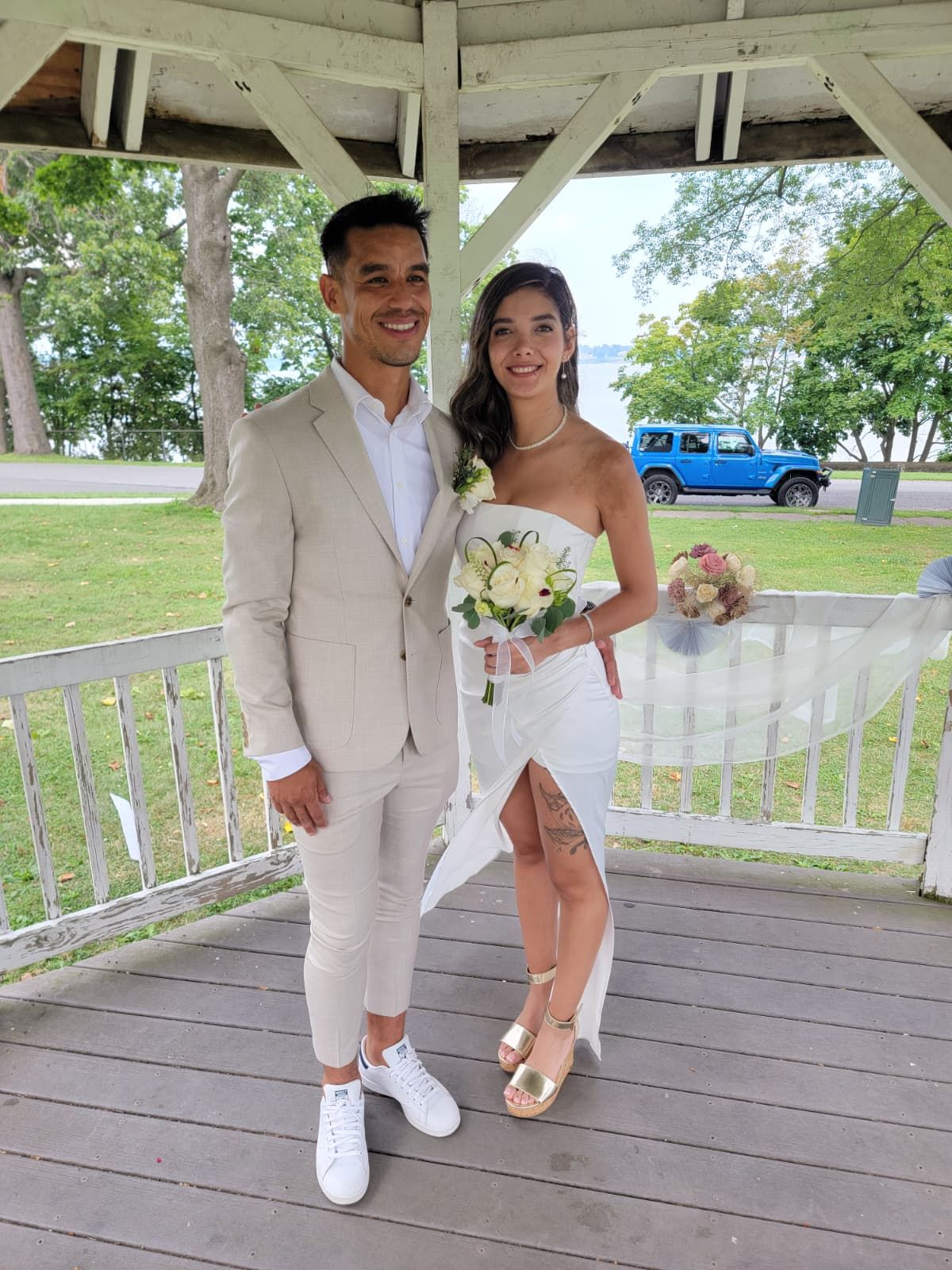 Bride and groom at a wedding, standing at a table. Backdrop with lights and floral accents.