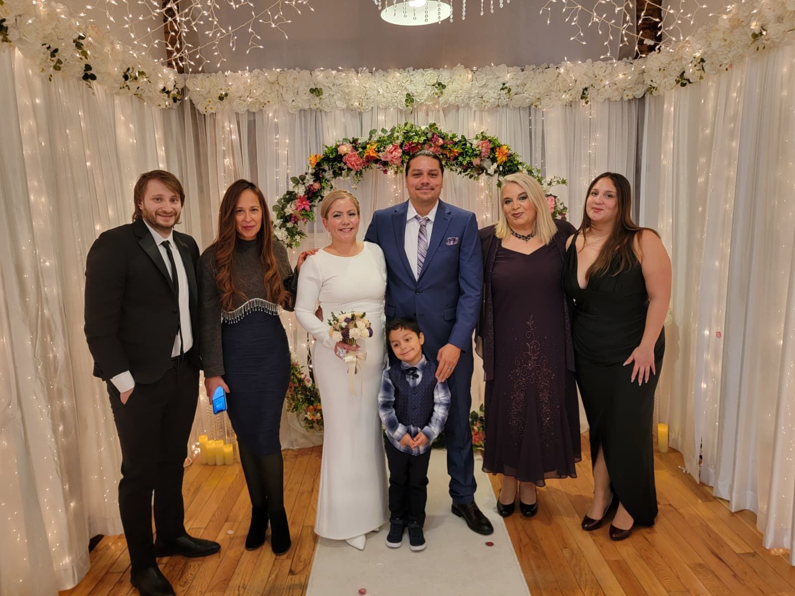 Couple kissing on wedding day, holding flowers, blue sky, bridge in background.