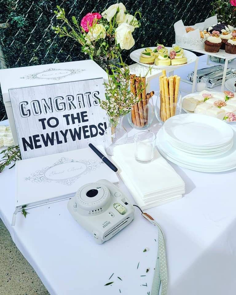 A wedding guest book table featuring a sign, a guest book, an instant camera, and hors d'oeuvres on a white tablecloth.