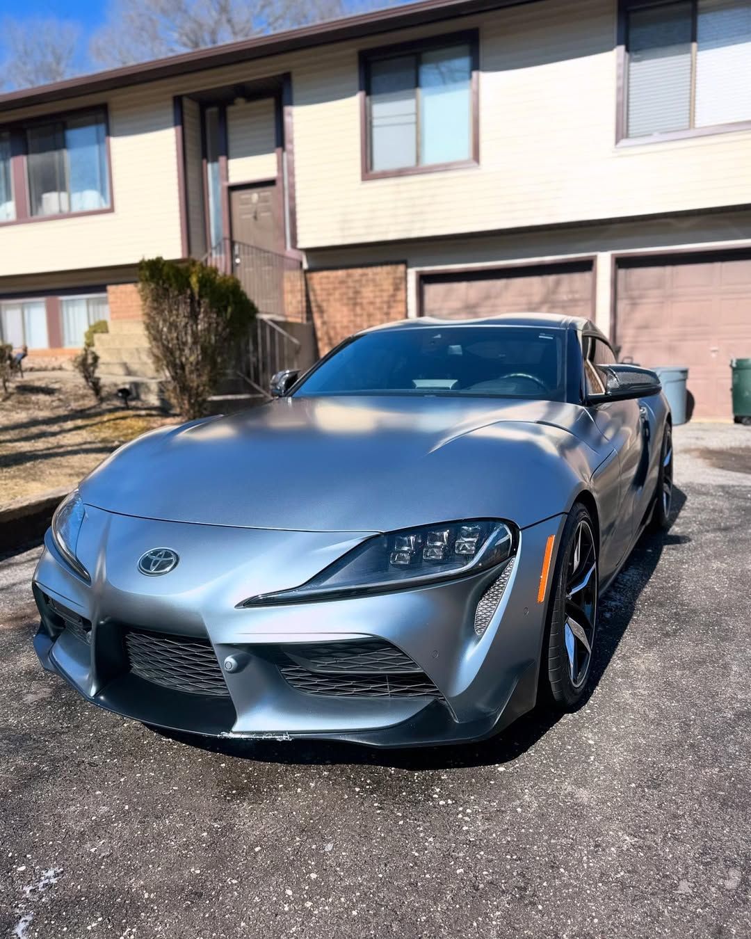 A silver sports car is parked in front of a house.