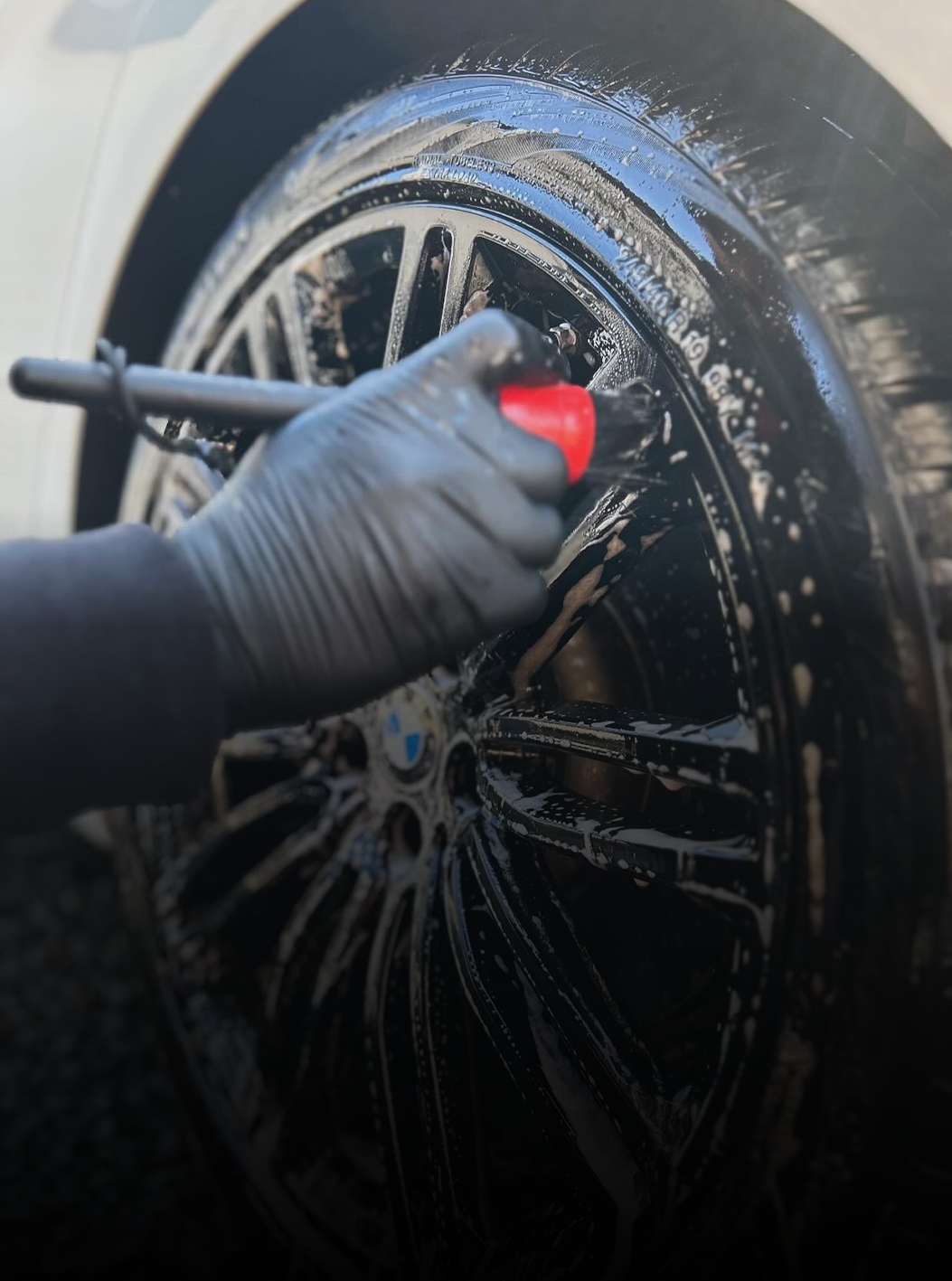 A person is cleaning a car wheel with a red brush.