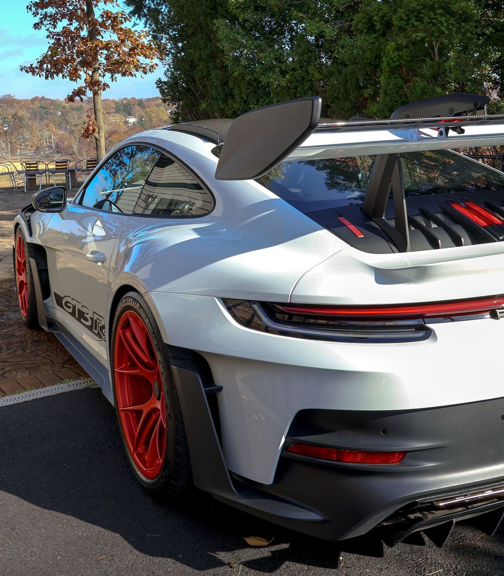A white Porsche 911 gt3 with red wheels is parked on the side of the road.