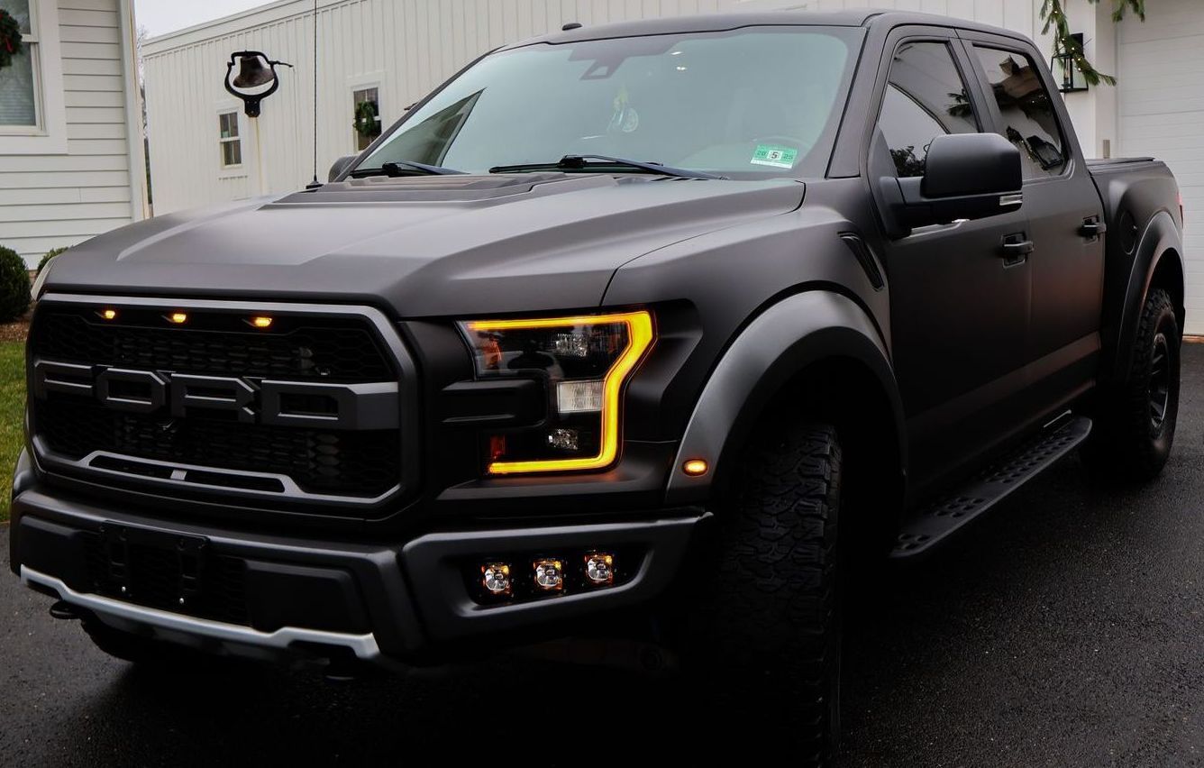 A black ford raptor truck is parked in front of a house.
