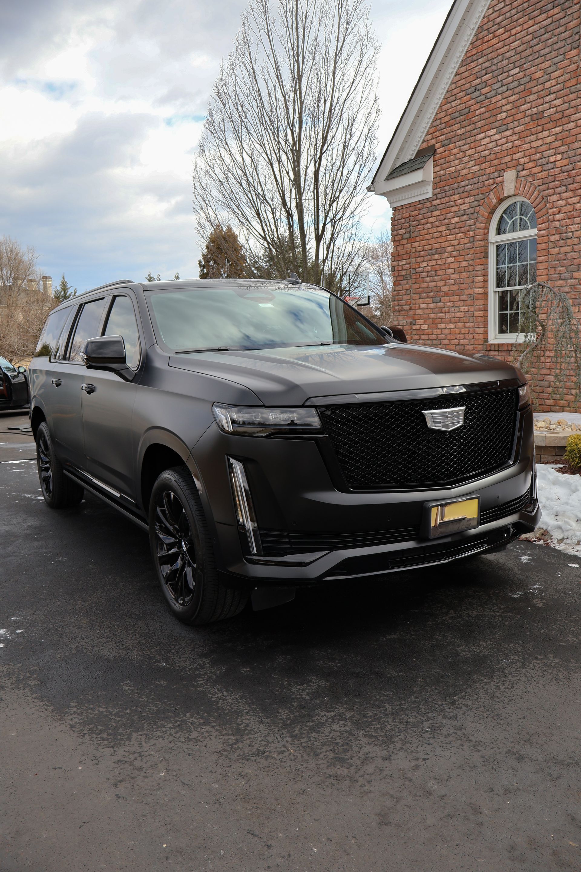A black cadillac escalade is parked in front of a brick building.