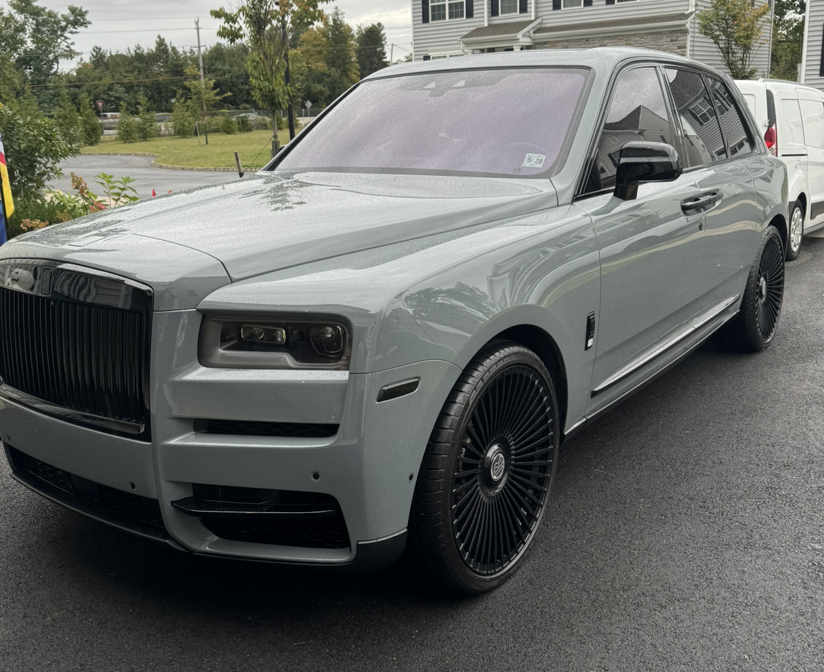 A gray rolls royce is parked in a driveway in front of a house.