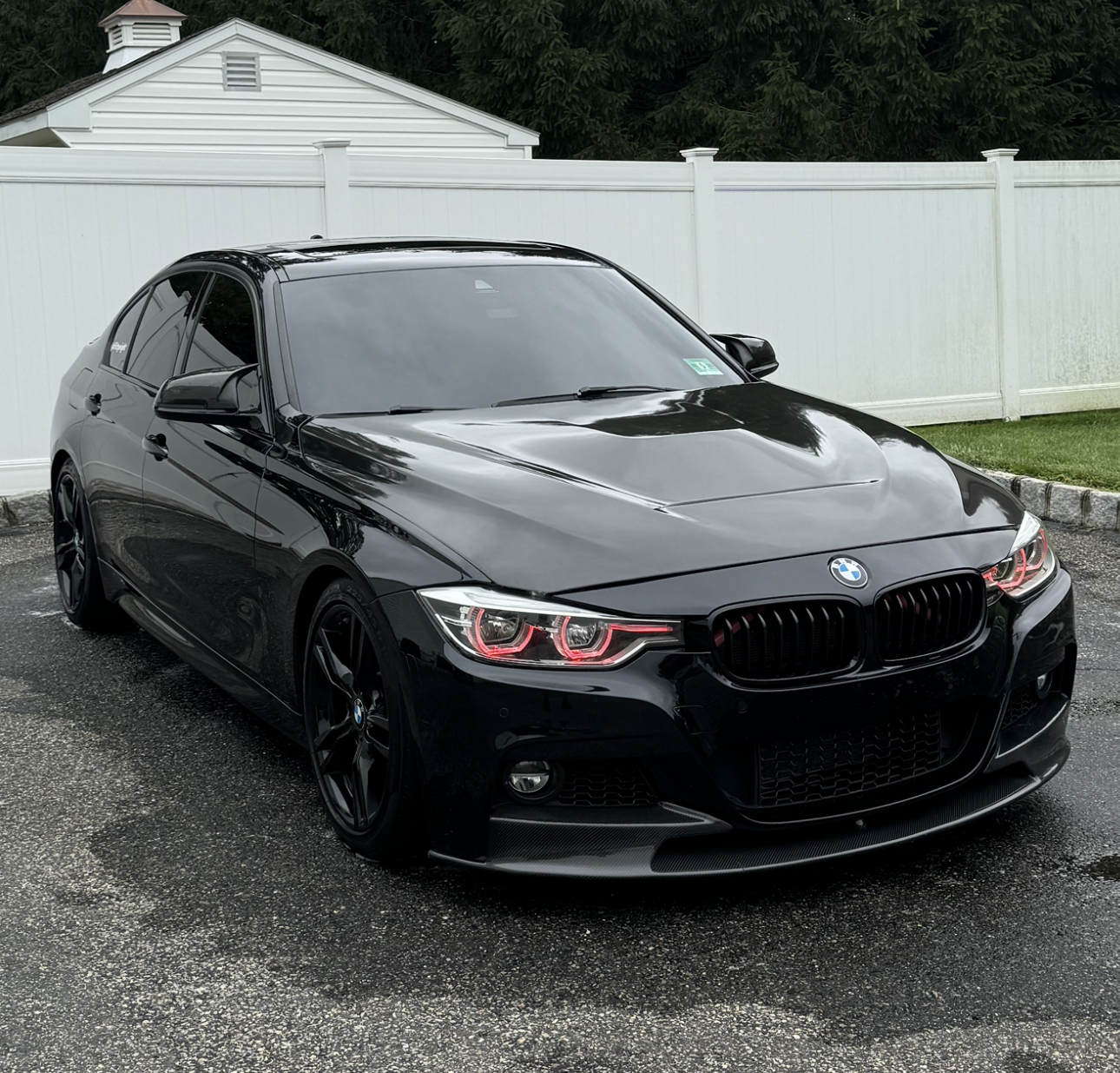 A black bmw F80 M3  is parked in front of a white fence.
