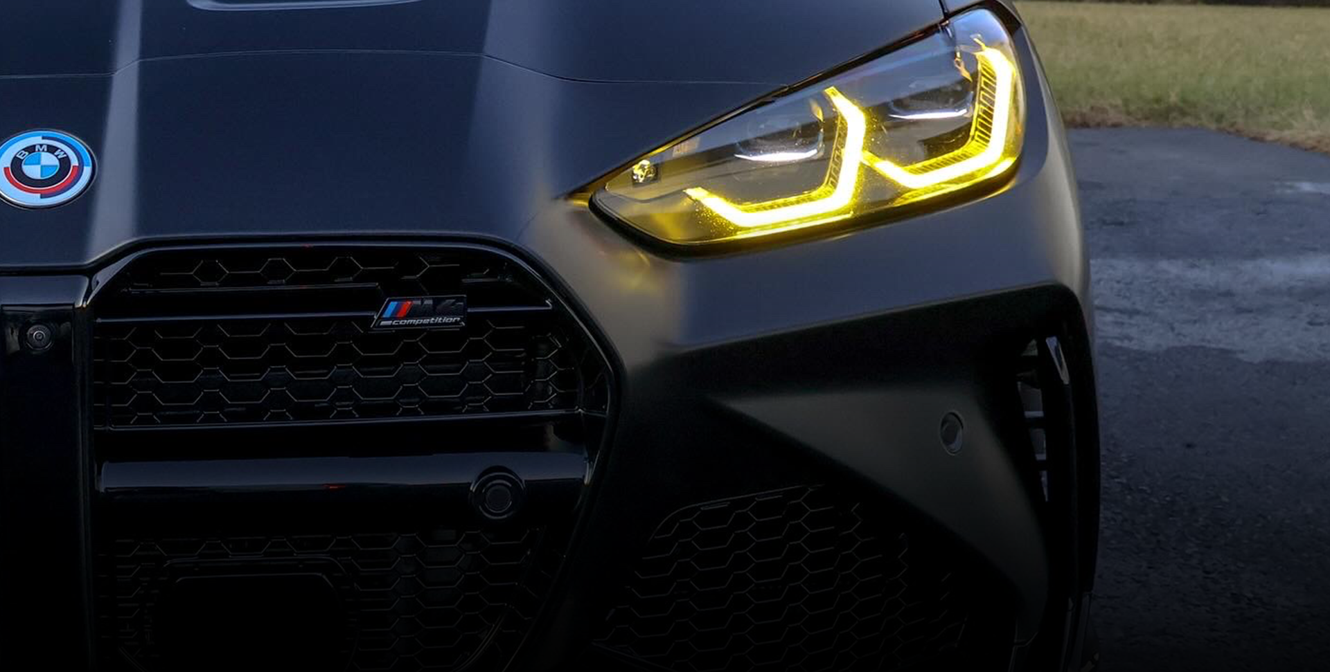A close up of the front of a black G82 M4 with yellow headlights.